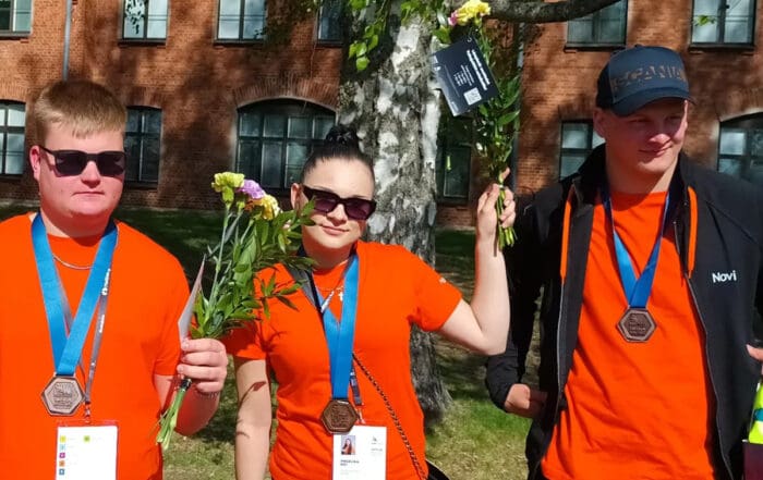 Valokuva kolmesta oranssipaitaisesta opiskelijasta jotka voittivat pronssia Taitaja 2024 ammattitaidon suomenmestaruuskilpailuissa Kuopiossa
